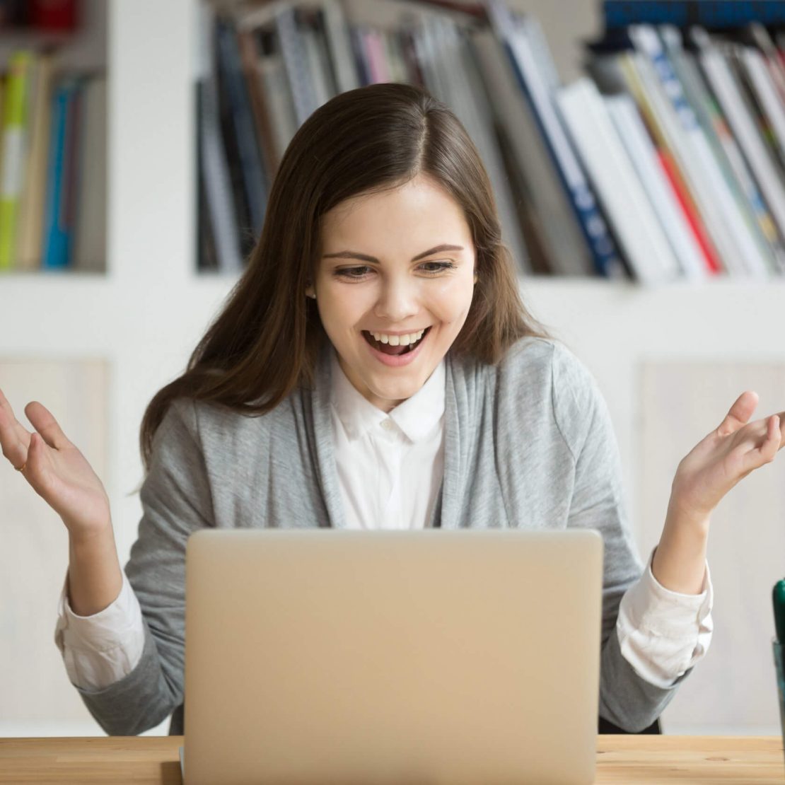 Happy young business woman looking at laptop computer screen in office